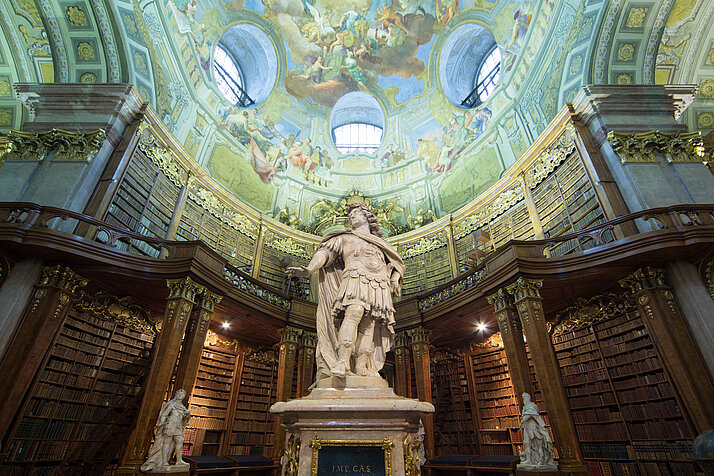 Fotografie des Prunksaals der Österreichischen Nationalbibliothek, mit einer zentralen Aufnahme der Statue von Kaiser Karl VI
