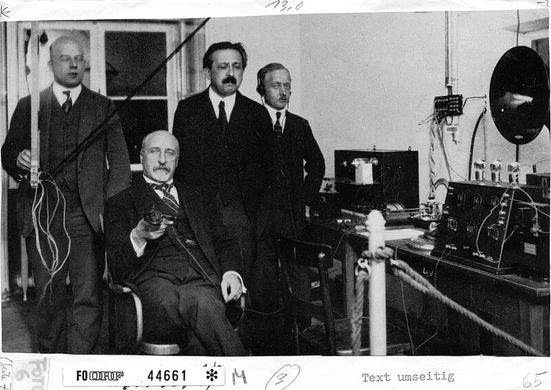 Schwarz-weißes Foto von vier Personen in Anzügen in einem altmodischen Aufnahmestudio.