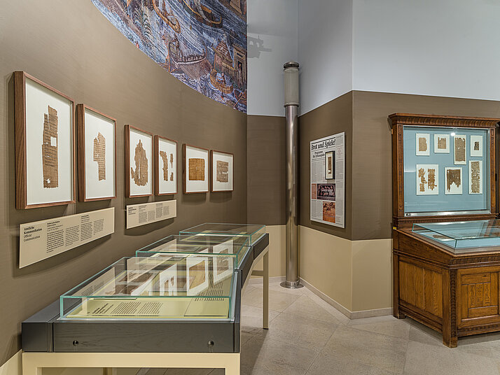 Blick in das Papyrusmuseum. Die Objekte hängen in Rahmen an der Wand und sind in Pultvitrinen ausgestellt.